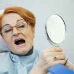 woman looks at teeth in the mirror